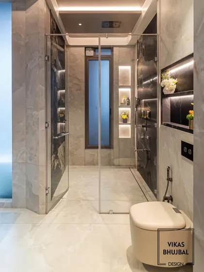 This bathroom design balances light and dark marble for a sophisticated contrast. The walk-in shower is framed by glass, and recessed, backlit niches provide elegant storage for toiletries.