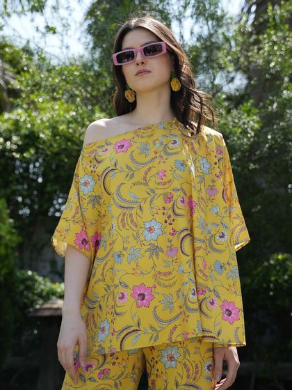 A bright yellow floral top and pants set, styled with modern pink sunglasses. The bold colors and sunny setting create a cheerful and eye-catching image for a summer campaign.