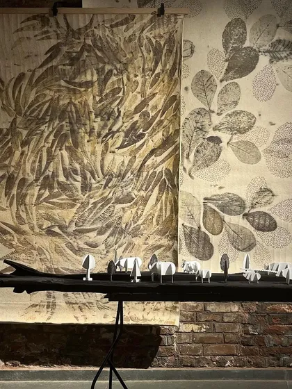 A piece from the 'Intersection' exhibit we curated, featuring a large wooden sculpture in front of two botanical-printed textile panels. The display highlights the dialogue between different materials and artistic practices.