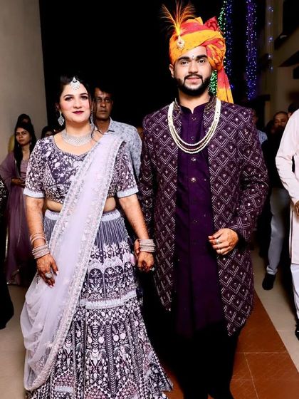 This groom chose a wine-colored open Lakhnavi Indo-Western jacket over a matching kurta. The outfit coordinates with the bride's lehenga, creating a harmonious look for their wedding event.