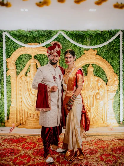 A formal portrait of the couple in their beautiful South Indian wedding attire, standing before a grand golden backdrop.