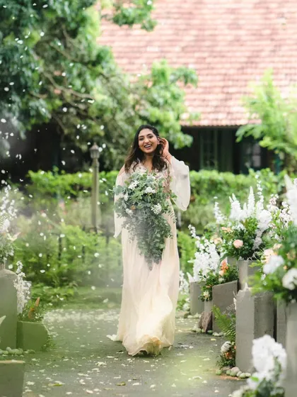 A bride's joyful entrance, walking down an aisle of petals in a beautiful garden setting. The soft light and lush greenery make this outdoor ceremony feel like a fairytale.