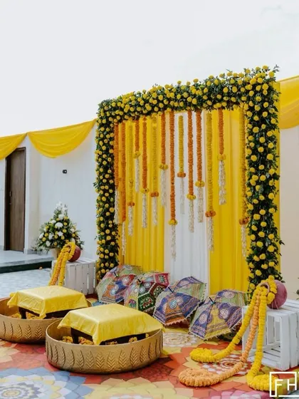 A beautiful and simple Haldi seating area with low stools placed in decorative baskets. The backdrop is a classic frame of marigolds with hanging floral strings, perfect for an intimate home ceremony.