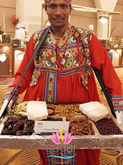 To bring a touch of nostalgia and tradition, I have servers in authentic regional attire offering classic snacks. This server is carrying a 'kavd' tray with favorites like roasted peanuts, chana, and tamarind candies.