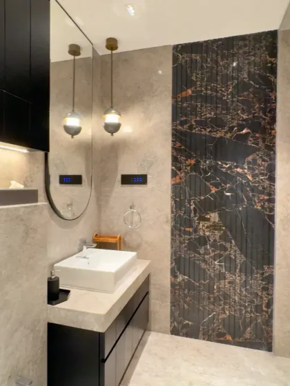 This bathroom combines classic and modern elements. A dark, fluted marble panel creates a dramatic accent wall behind the sink, while minimalist pendant lights and a sleek vanity complete the sophisticated look.