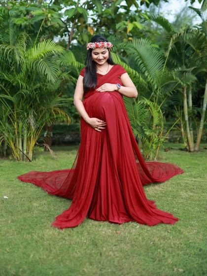 A client cradling her bump in a wine-colored A-line gown, surrounded by lush greenery. The soft, flowing fabric and rich color make this a beautiful choice for nature-themed photoshoots.