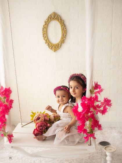 Two sisters sitting together on a floral swing. This setup creates a whimsical and beautiful setting for sibling portraits.