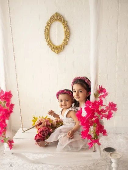 Two beautiful sisters sitting on our studio swing. The bright flowers and their sweet interaction create a whimsical and lovely sibling portrait.
