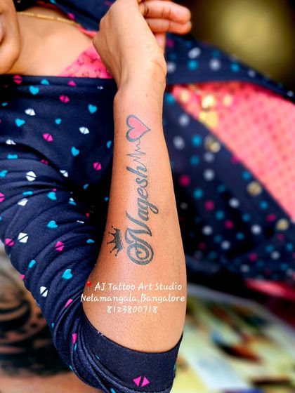 A "Nagesh" name tattoo with a crown and heartbeat line, a popular combination.