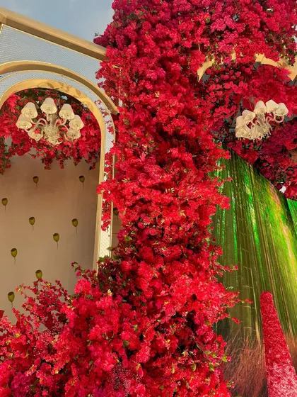 A close-up of the vibrant red floral installations. The modern chandeliers inside the arches add a touch of glamour and light to the intensely colorful decor.