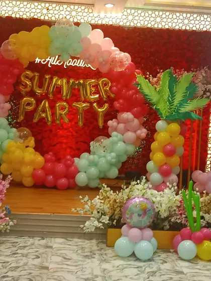 A tropical summer party theme with a colorful balloon ring. The setup includes foil letters spelling 'Summer Party' and balloon sculptures of a palm tree and a unicorn.