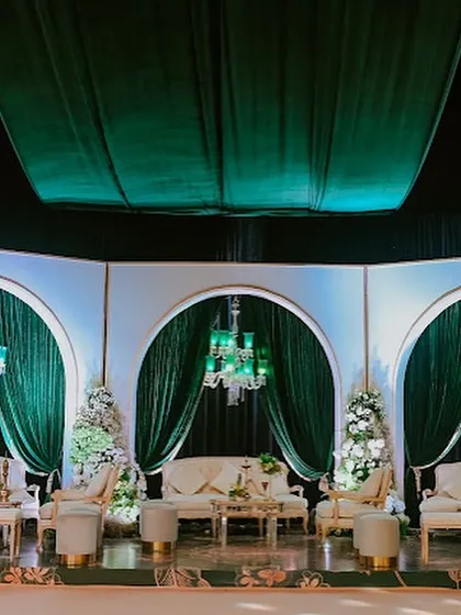 The stage-side lounge area, featuring elegant white sofas set against a backdrop of three grand arches draped in emerald velvet and lit by green chandeliers.