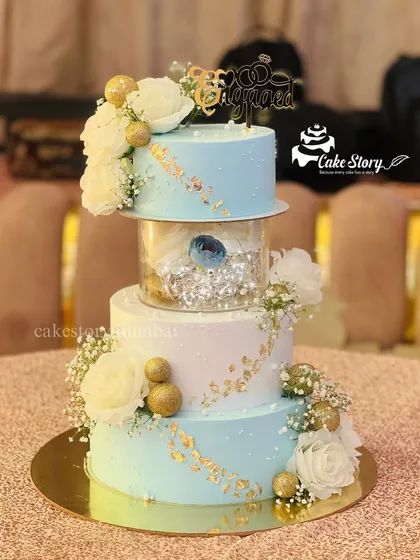 For a beautiful engagement, I designed this elegant three-tier cake. It features a soft blue and white palette, delicate white flowers, and touches of gold leaf for a sophisticated look that celebrates a new beginning.