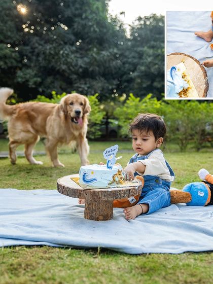A classic cake smash scene with a furry twist. As baby Aariv digs into his first birthday cake, his loyal Golden Retriever, Ollie, watches on, hoping for a share. This is a fun and memorable way to include pets in milestone celebrations.