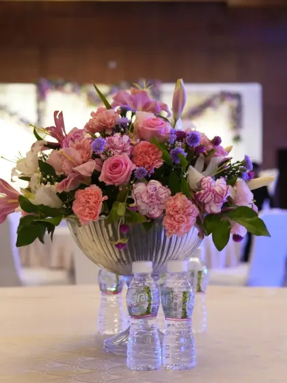 A beautiful floral centerpiece for a formal dinner, featuring a mix of pink roses, lilies, and carnations. Such arrangements add a touch of softness and elegance to the tables.
