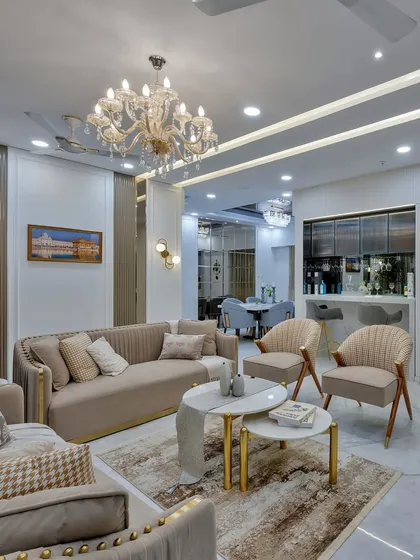 Luxury and comfort coexist in this elegant living space. A grand crystal chandelier adds a touch of glamour, while the plush, neutral-toned furniture and soft rug create a warm and inviting atmosphere for relaxation.