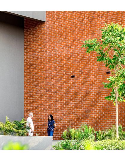 A close-up of the material palette at SWAJAN, showing the interplay between the warm red brick wall and the smooth grey render. The presence of residents and staff highlights the project's human-centric approach.