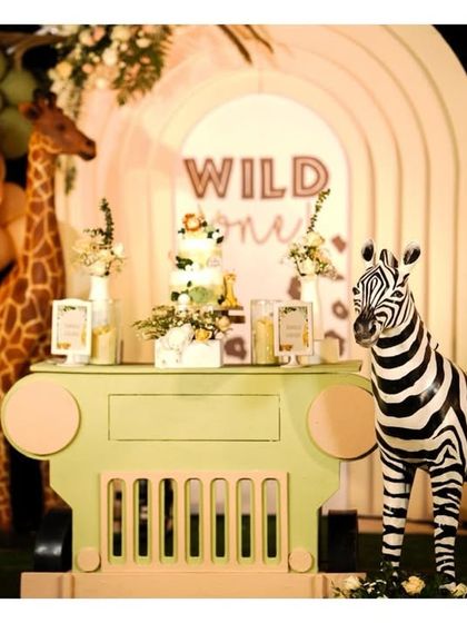 A full view of the dessert table from our pastel jungle party, featuring a custom-built safari jeep stand, flanked by a tall giraffe and a friendly zebra, all under a canopy of lush balloon garlands.