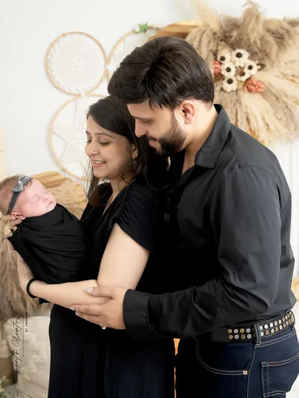 A quiet moment with a new family. The parents, dressed in black, look down at their sleeping newborn daughter, creating a simple and intimate portrait.
