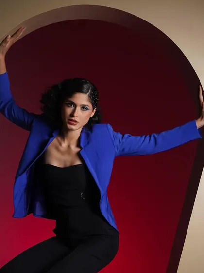 A bold and graphic studio portrait using contrasting colors and a strong pose. The vibrant blue jacket against the red background creates a high-impact visual, ideal for a fashion campaign that needs to stand out.