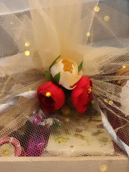 A close-up of a beautifully wrapped Diwali gift hamper, showing the delicate net packaging and floral decoration.