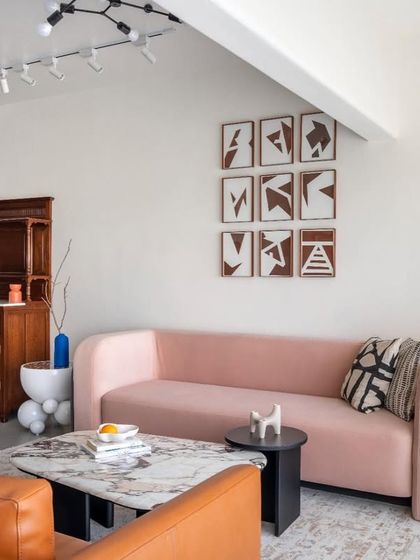 This living area is a study in balancing forms and colors. The custom pink sofa with its curved silhouette is set against a gallery wall of abstract art, while a vintage wooden cabinet adds a touch of history. The space feels curated, personal, and full of character.