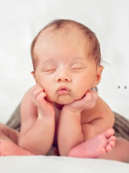 The classic 'froggy' pose is a favorite among parents. It requires patience and careful handling to safely position the baby, highlighting their delicate features and curled-up form against a simple, pure white backdrop.