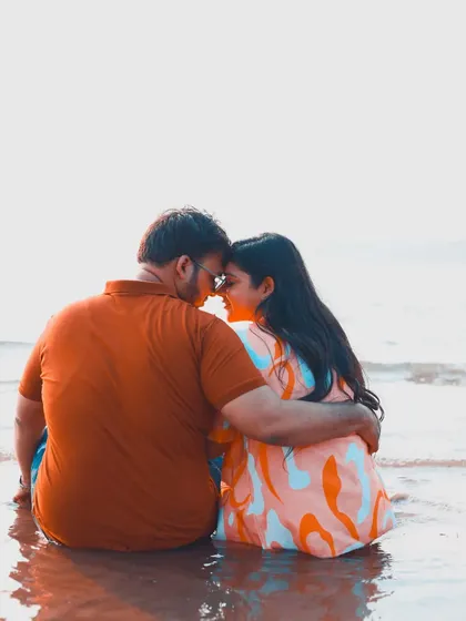A tender moment of a couple sitting in the water at the beach, with a bright, minimalist background.