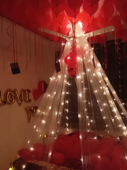 A romantic anniversary surprise with a canopy over the bed. The setup is filled with red balloons and "I LOVE YOU" foil letters.