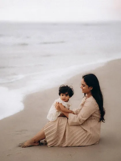 A mother and her baby sit by the water's edge, sharing a peaceful moment as the waves gently roll in. This serene image is a beautiful example of a natural and relaxed mother-child photoshoot.