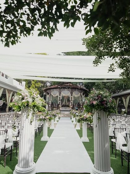 A grand wedding aisle with white pillars and floral arrangements leading to the bandstand.