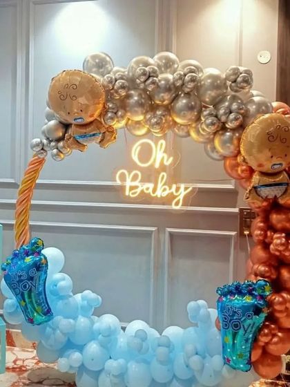 A modern "Oh Baby" baby shower theme with a unique color combination. This circular balloon arch uses chrome silver, bronze, and light blue balloons, with a neon sign and baby-themed foils.