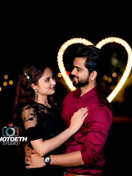 A beautiful nighttime couple portrait with a softly lit heart in the background. The bokeh effect from distant lights adds a dreamy quality to the image.