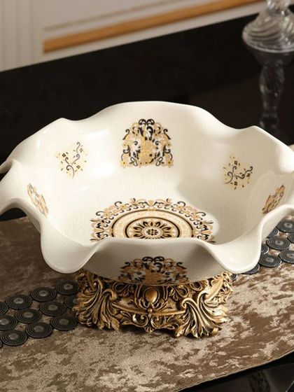 This elegant serving bowl features a beautiful scalloped edge and a base with intricate, antique-gold detailing. The interior is adorned with classic patterns, making it a perfect piece for stylish entertaining.