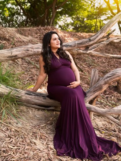 A serene portrait of the mother-to-be seated on a fallen log in the woods. The deep purple of her gown provides a beautiful contrast to the natural, earthy tones.