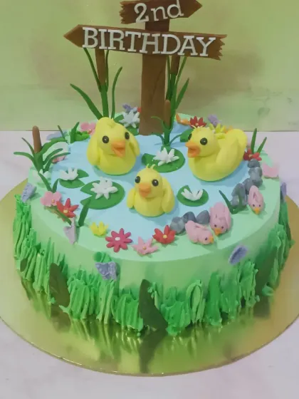 A charming duck pond cake for a 2nd birthday. This cake features little yellow fondant ducks swimming in a blue "pond" surrounded by green buttercream "grass."