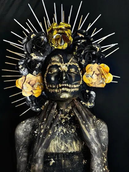 A dark fantasy look with a black and gold color scheme, featuring a skull illusion and a floral headpiece.