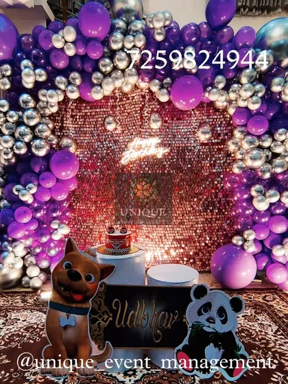 A birthday decoration set up at home with a purple and silver theme. It features a sparkling sequin backdrop, a balloon arch, and cute animal cutouts, showing how we can create a festive party atmosphere in any space.