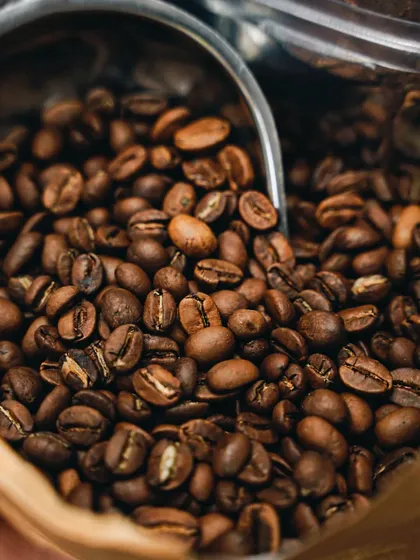 Nothing like the smell of fresh coffee. A close-up shot of roasted coffee beans in a bag with a scoop, capturing the rich brown color and texture. Shot for a local cafe.