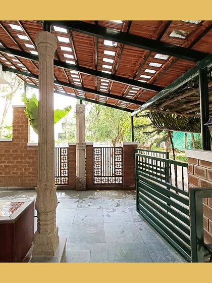 A welcoming verandah with traditional stone pillars and a sloping roof with exposed tiles, overlooking a garden.