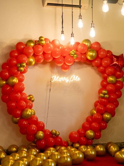 Our heart-shaped balloon arch is a popular choice for proposals. Made with vibrant red and gold balloons, it frames the moment perfectly and includes a 'Marry Me' neon sign at its center.
