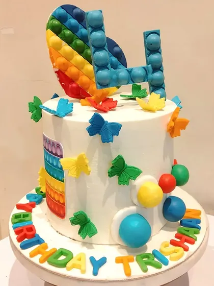 A trendy and colourful pop-it themed cake. This design incorporates the popular fidget toy into the cake itself, with edible bubbles and a rainbow heart topper.