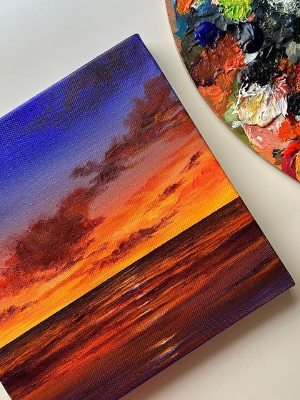 The vibrant sunset painting displayed next to my paint palette, showing the colors I used to create the piece.