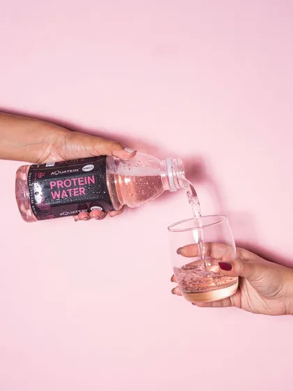 An action shot against a clean pink background. The pouring action adds dynamism and highlights the drink's refreshing, clear quality.
