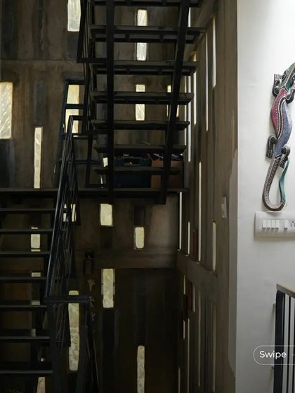 The industrial-style metal staircase in the Manjunath Residence, with light filtering through slits in the concrete wall, creating a dramatic and moody effect.