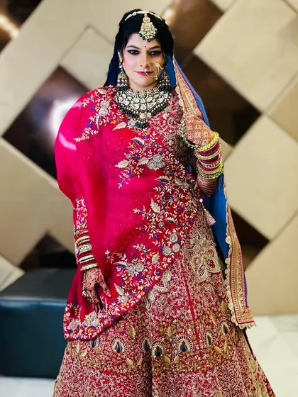 A full-length shot of a bride in a magnificent red and blue lehenga. This photo captures the grandeur of her complete bridal look, from head to toe.