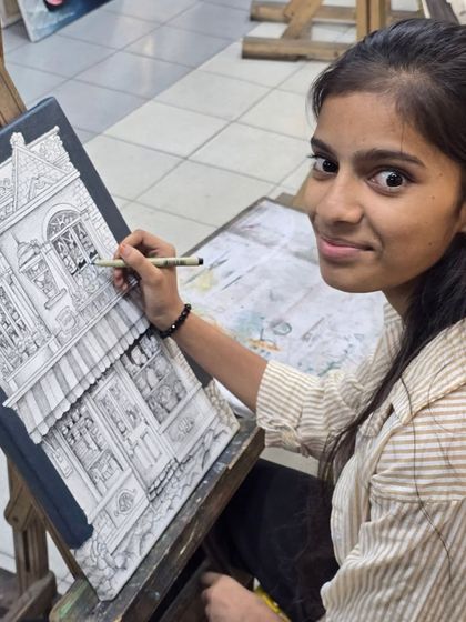 A smiling artist looks up from her work, giving a glimpse into the enjoyable and rewarding process of creating detailed ink drawings in our studio.