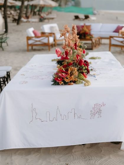 A long view of the beachside dining setup, with the custom-illustrated table runner telling the couple's story.