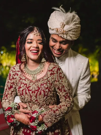 A joyful candid shot of the bride and groom. Her radiant makeup and stunning red lehenga with a long trail create a picture-perfect wedding memory.