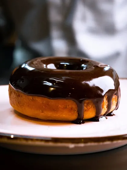 The perfect chocolate drip on a freshly fried doughnut. This shot is all about capturing that single, mouth-watering moment of action that makes a dessert irresistible.